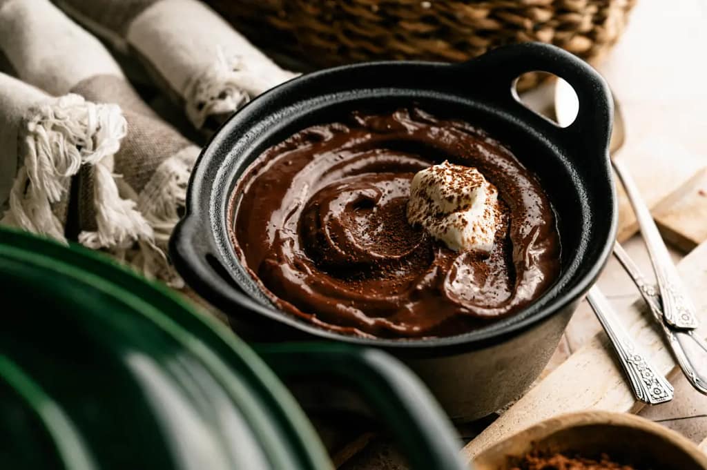Homemade chocolate pudding being garnished in a black serving bowl