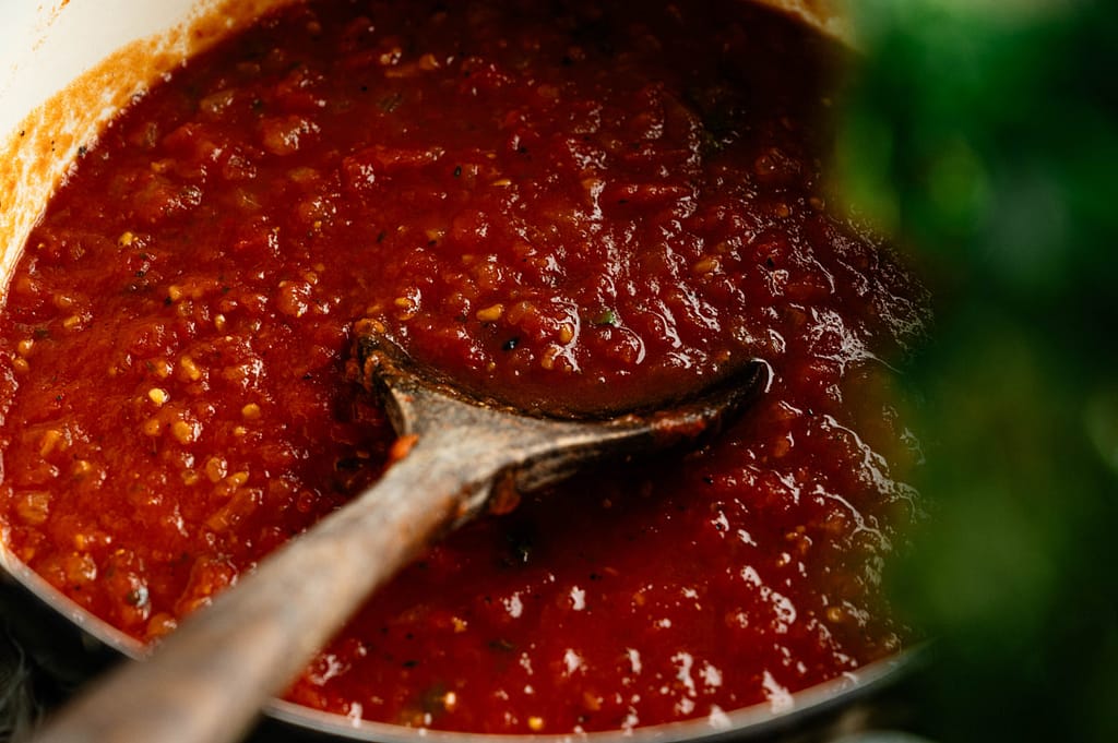 Wooden spoon stirring rustic homemade marinara sauce in a pot