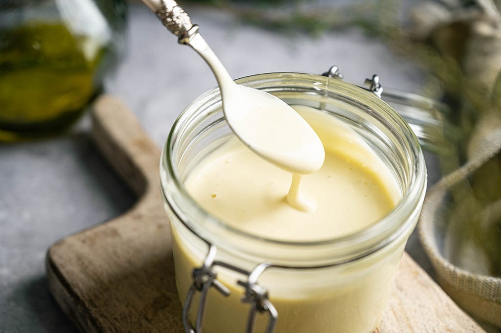 Mayonnaise falling from a raised spoon into an open glass jar