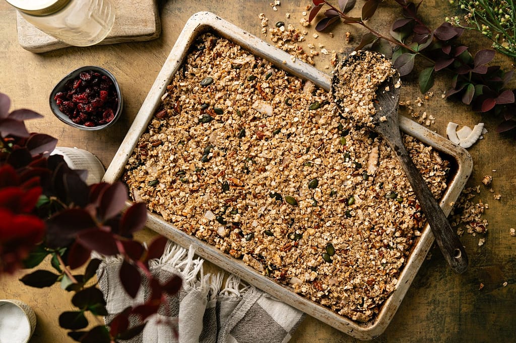 Unbaked oat, nut, seed, and coconut granola spread evenly across a parchment-lined baking sheet.