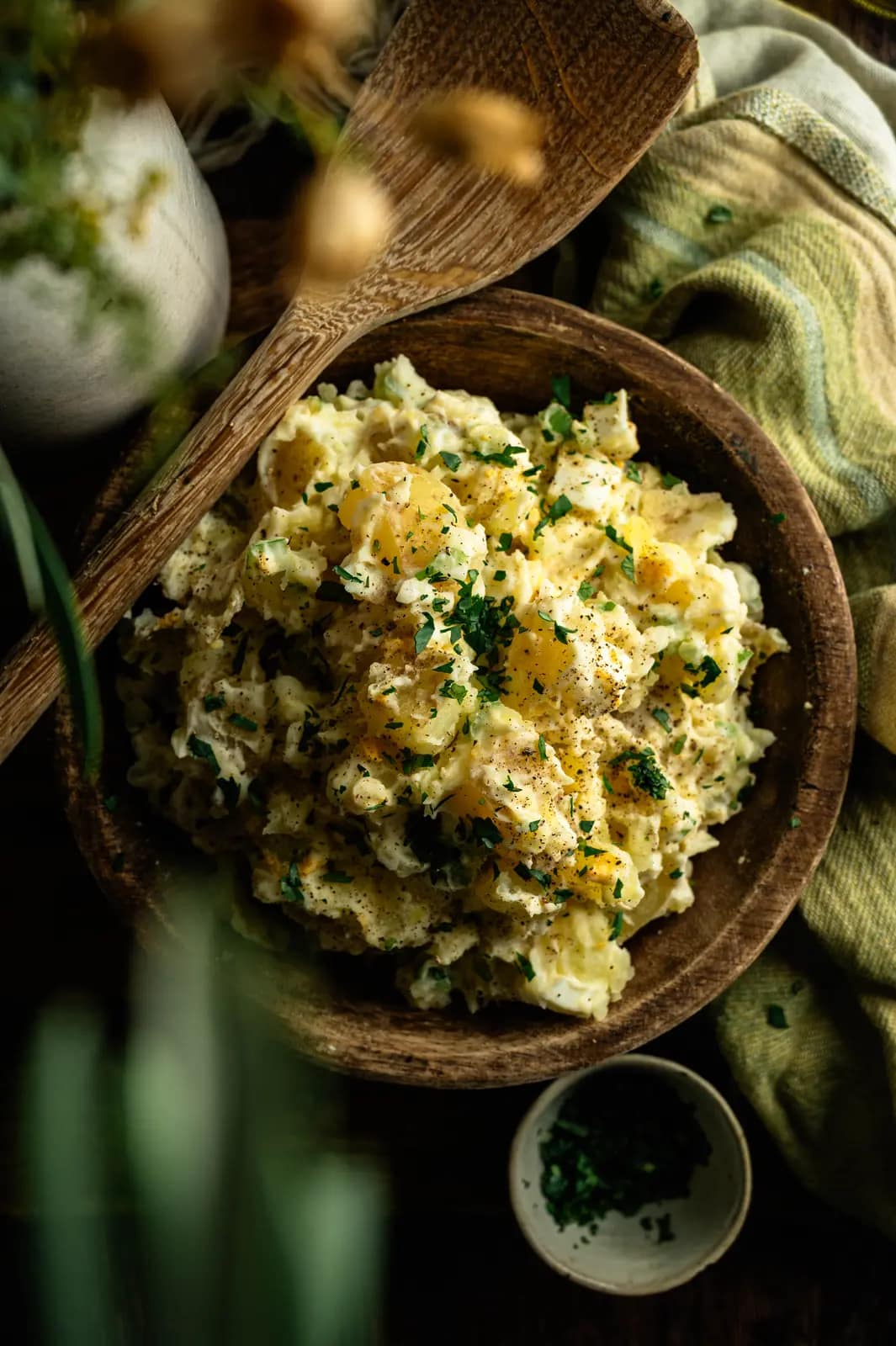 Creamy potato salad in a wooden bowl with green linen and serving utensils