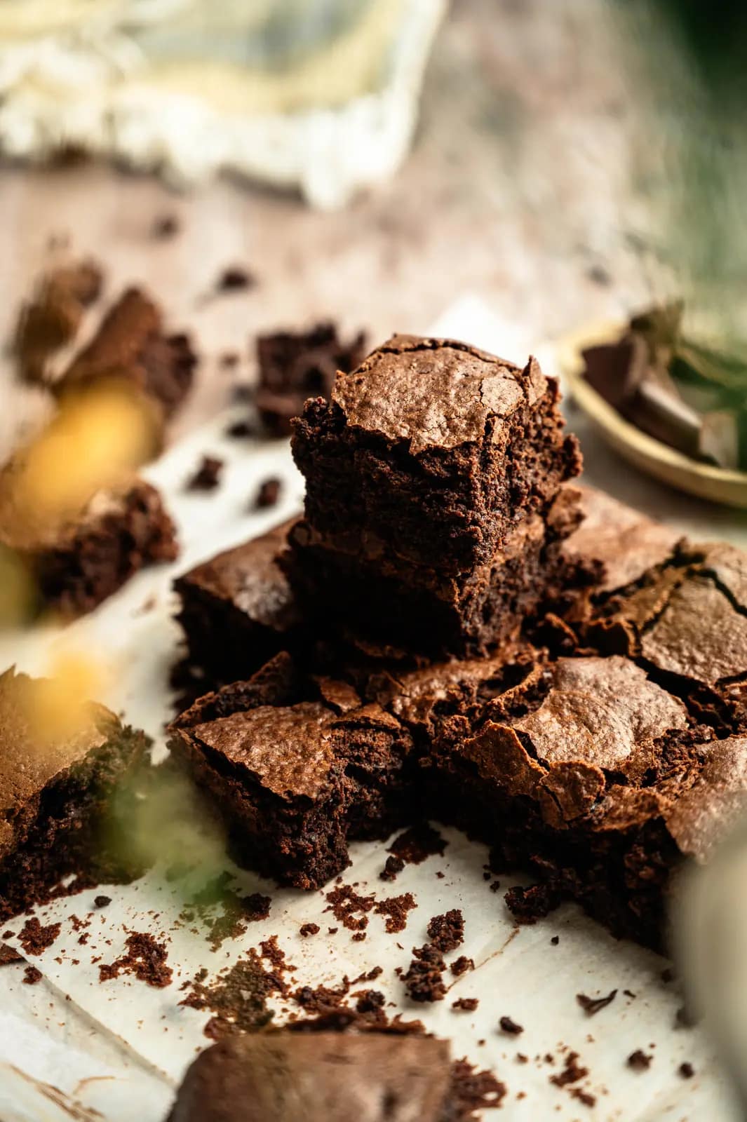 A tall stack of brownies on parchment surrounded by cut squares and chocolate crumbs.