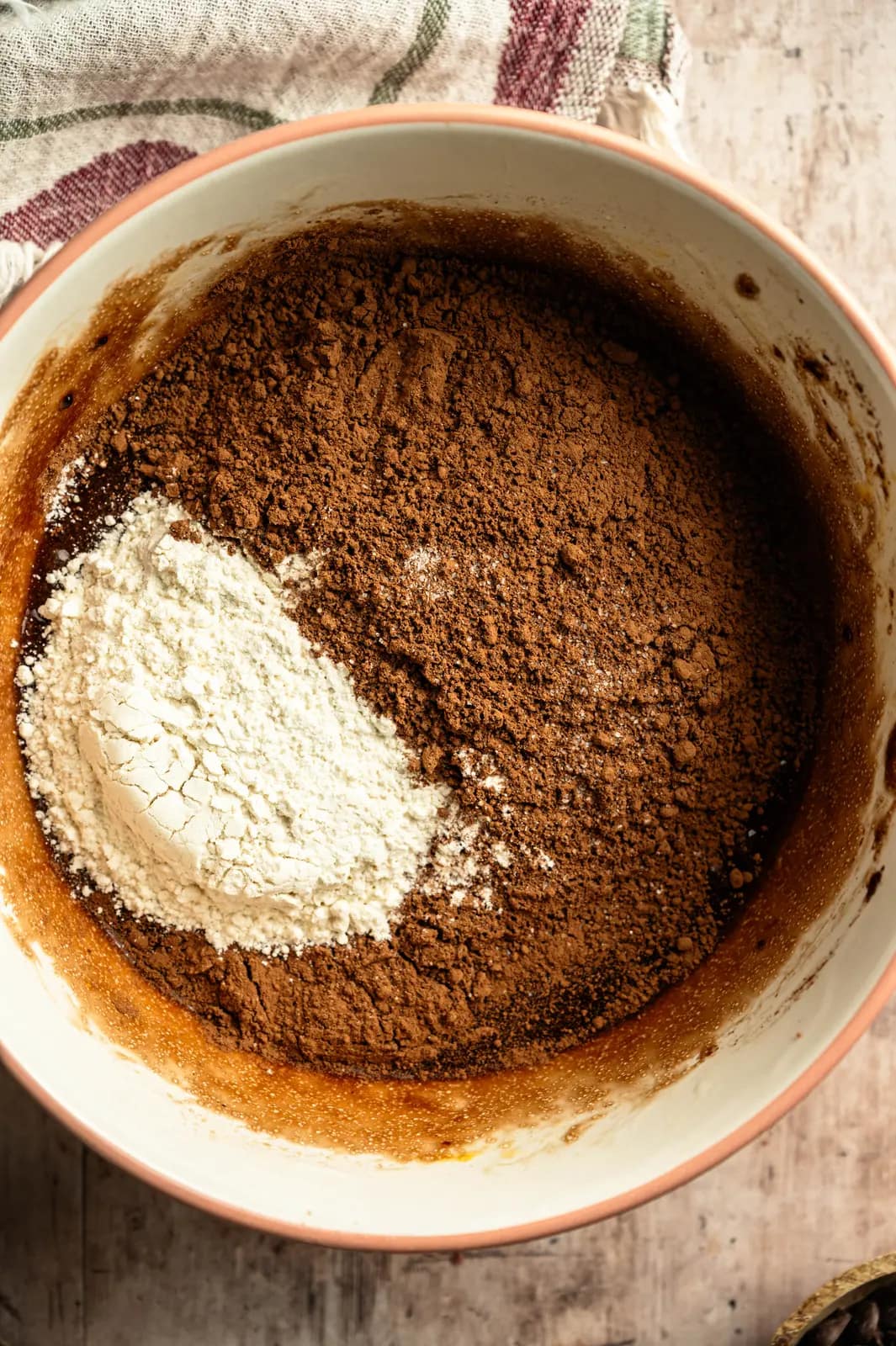 Flour and cocoa powder sitting on top of chocolate batter in a mixing bowl.
