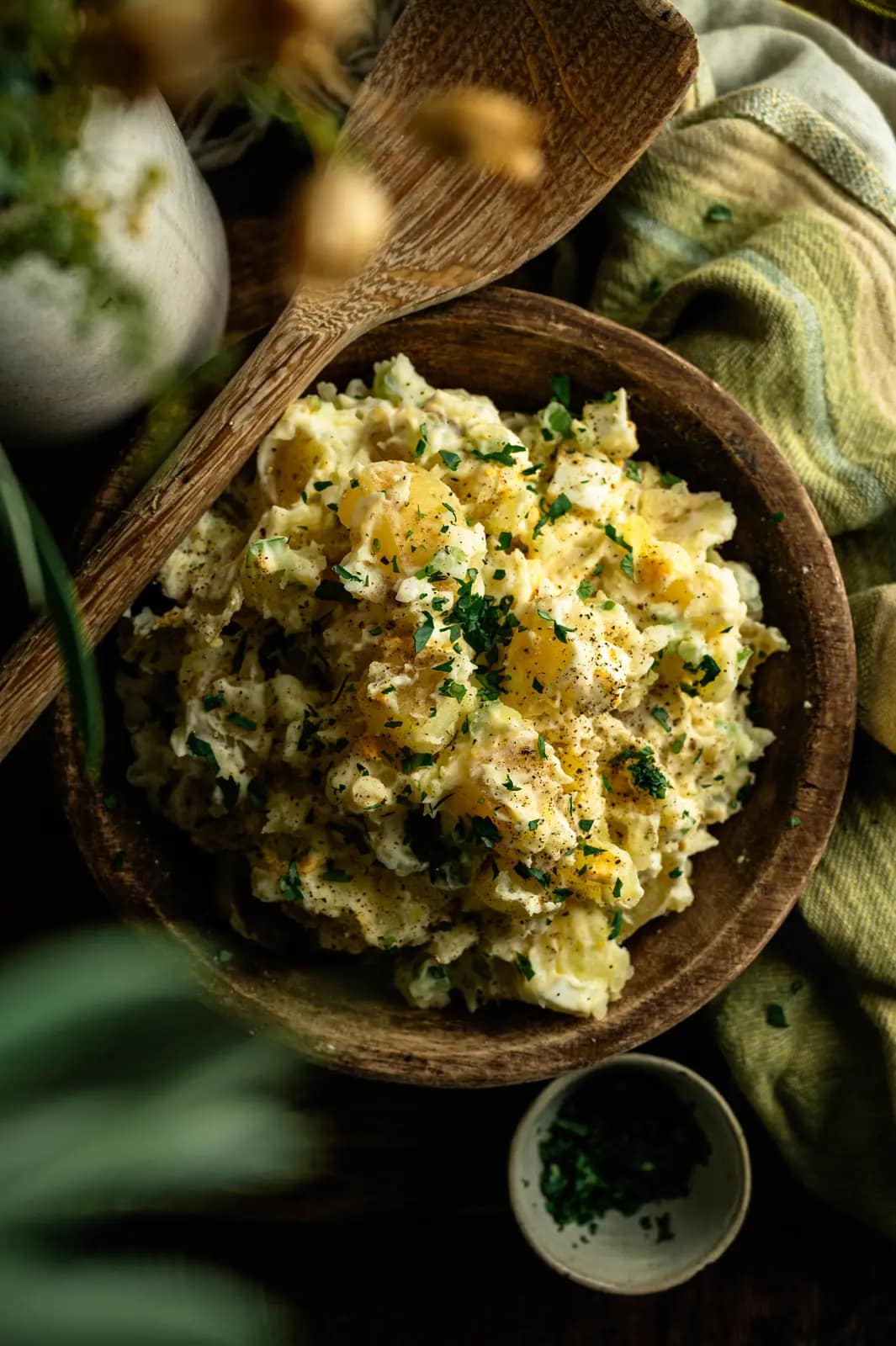 Overhead creamy potato salad garnished with herbs and black pepper in a wooden bowl
