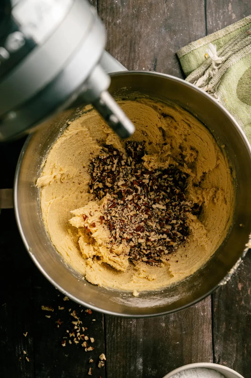 Chopped pecans added to snowball cookie dough in a metal mixer bowl.