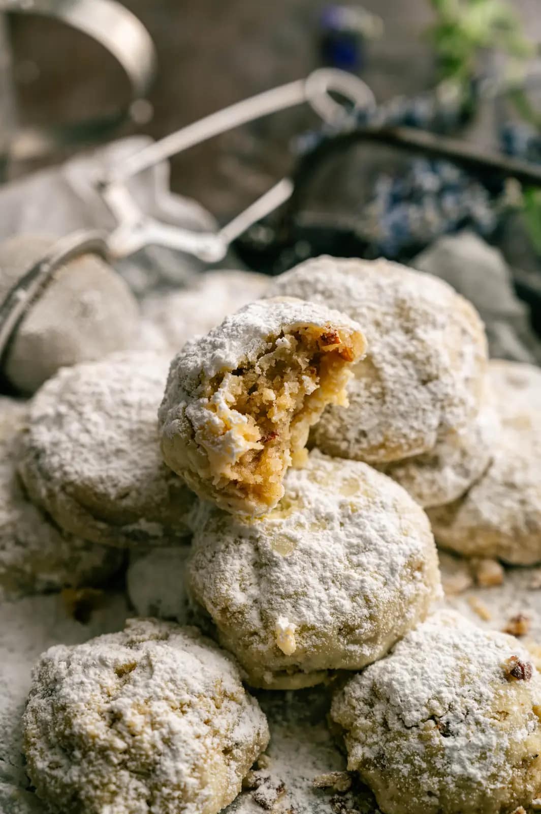 A broken pecan snowball cookie reveals its golden nut-filled center among sugar-coated cookies.