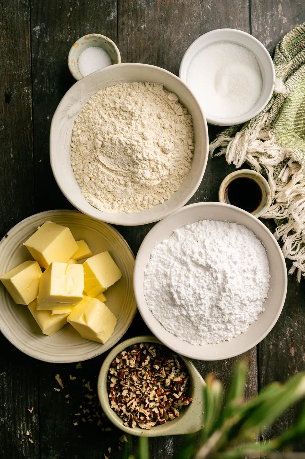Butter, flour, powdered sugar, chopped pecans, and vanilla arranged for snowball cookies.