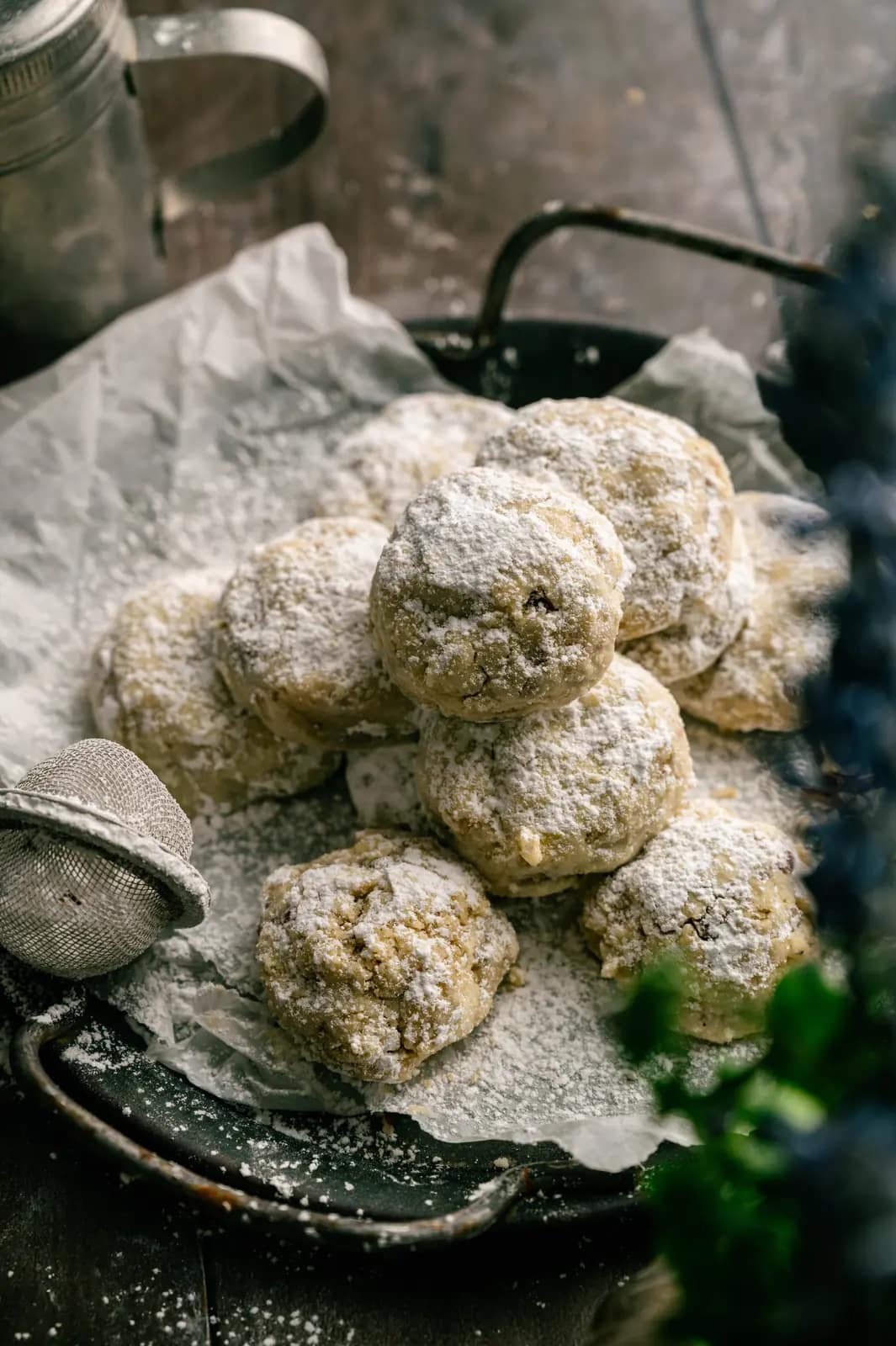 Pecan snowball cookies coated in powdered sugar on a parchment-lined dark tray.