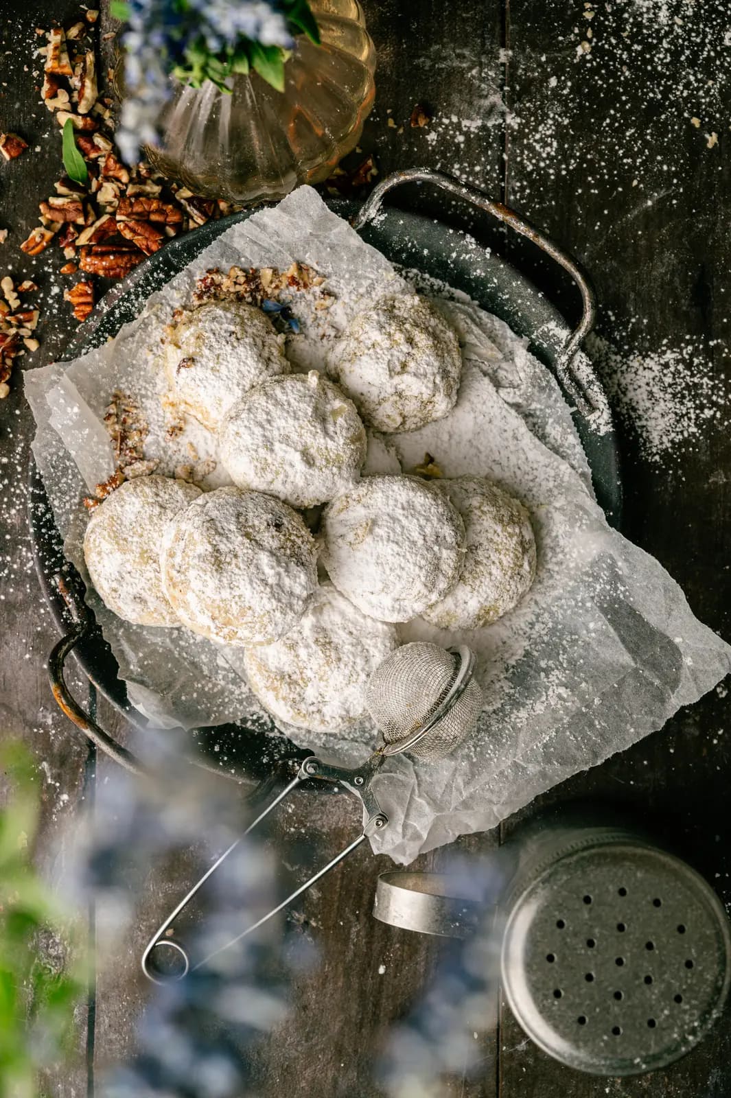 Pecan snowball cookies coated in powdered sugar on a parchment-lined dark tray.