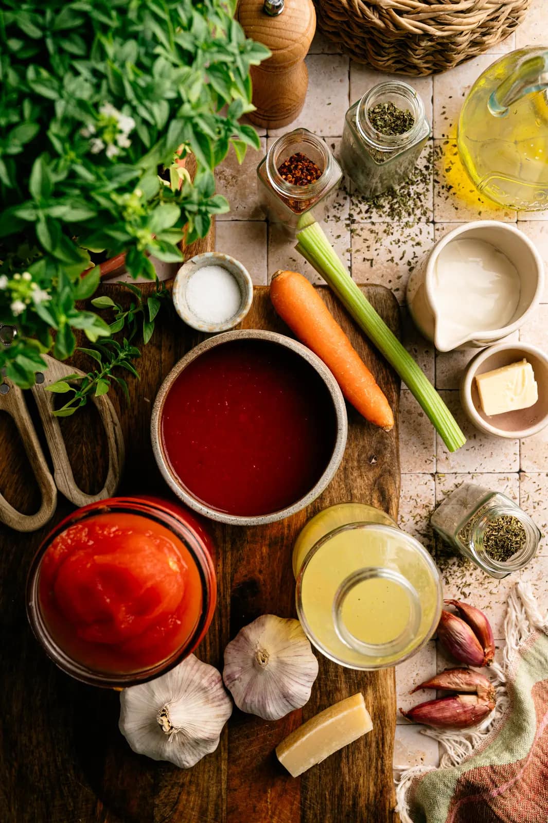 Tomatoes, carrots, celery, garlic, herbs, and other soup ingredients arranged on a wooden table.