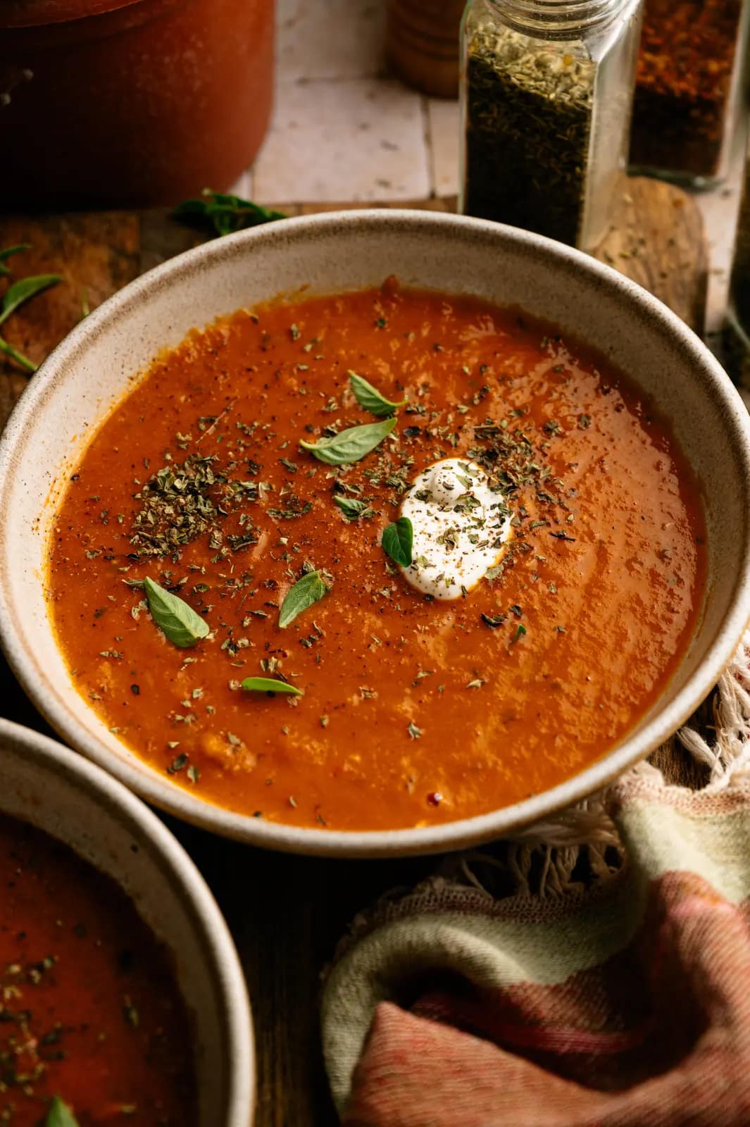 Rustic tomato basil soup topped with herbs and a dollop of cream in a ceramic bowl.