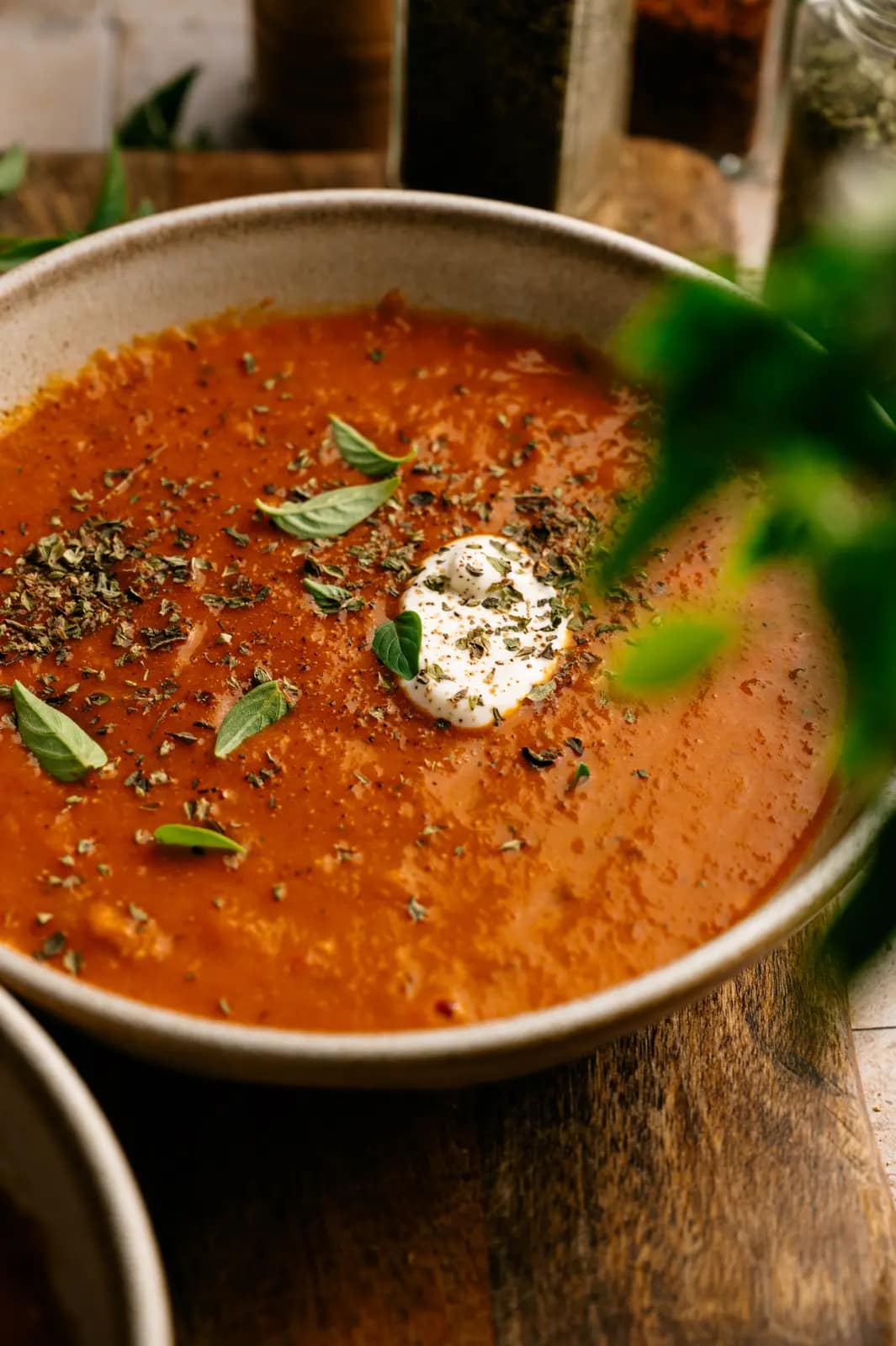 Rustic tomato basil soup topped with herbs and a dollop of cream in a ceramic bowl.