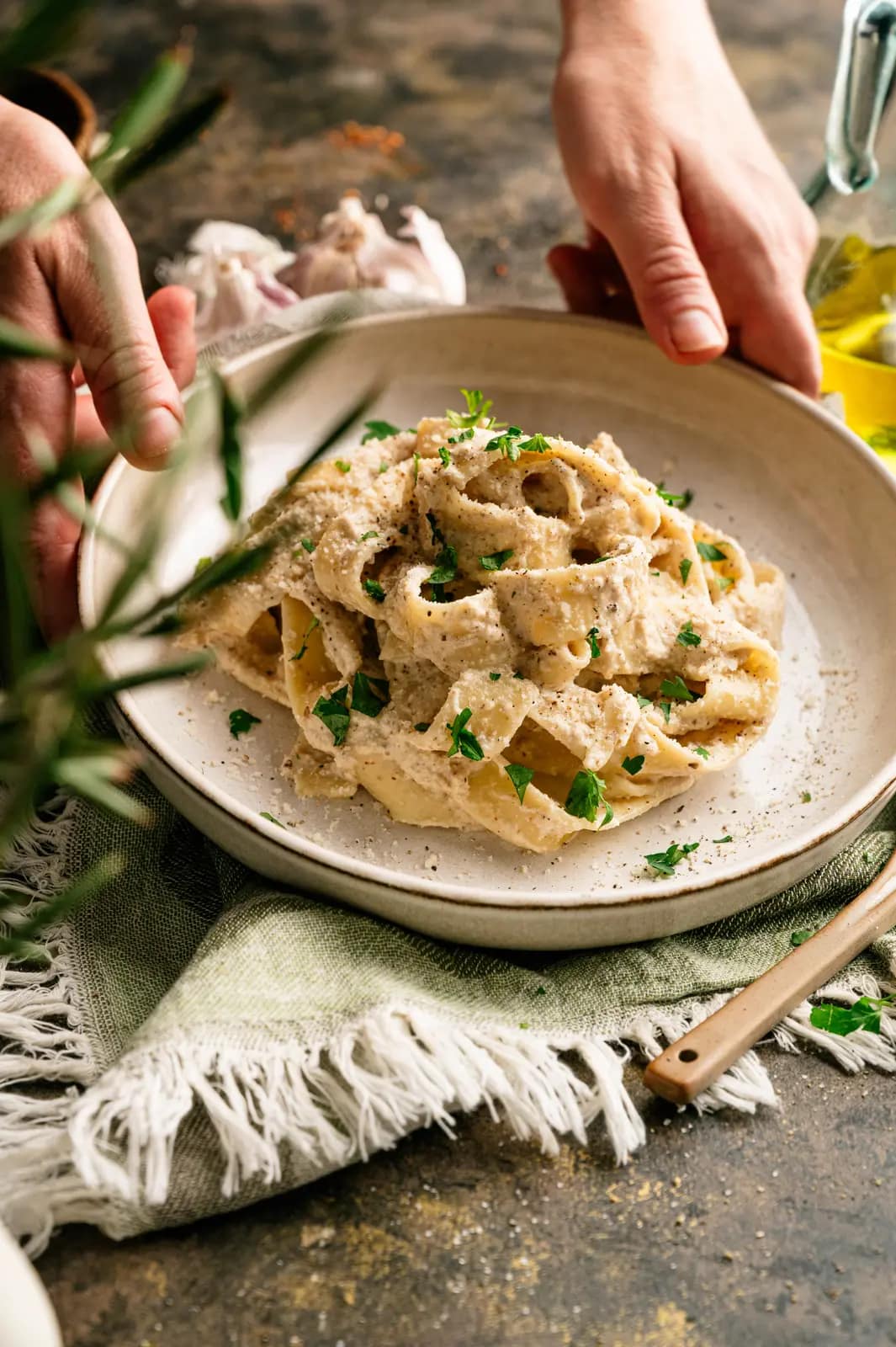 Hands setting down a plate of pasta coated in creamy Italian walnut sauce.