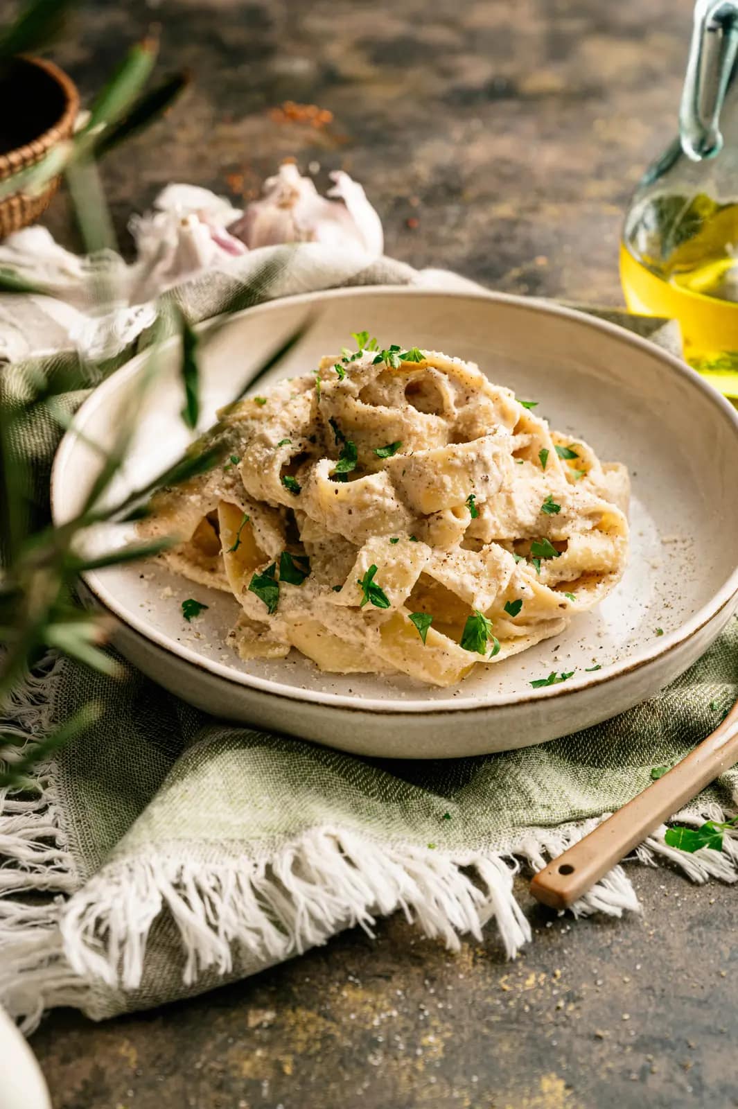 Ribbon pasta coated in creamy walnut sauce on a pale ceramic plate beside garlic and olive oil.