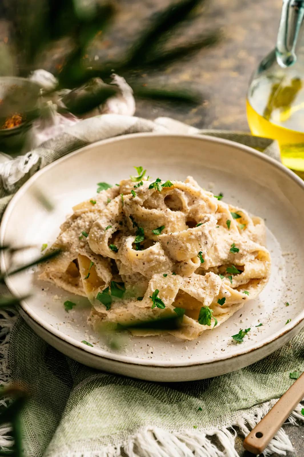 Ribbon pasta coated in creamy walnut sauce on a pale ceramic plate beside garlic and olive oil.