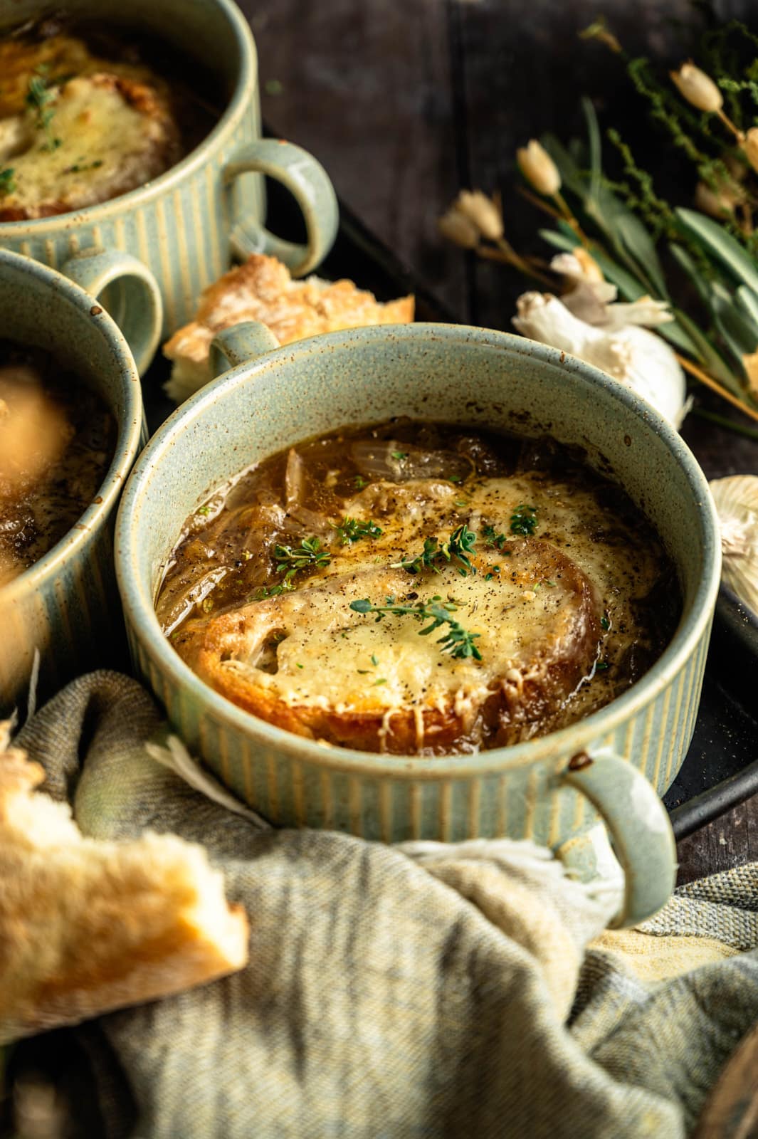 French onion soup topped with golden melted cheese and thyme in a green crock, with another bowl behind it.