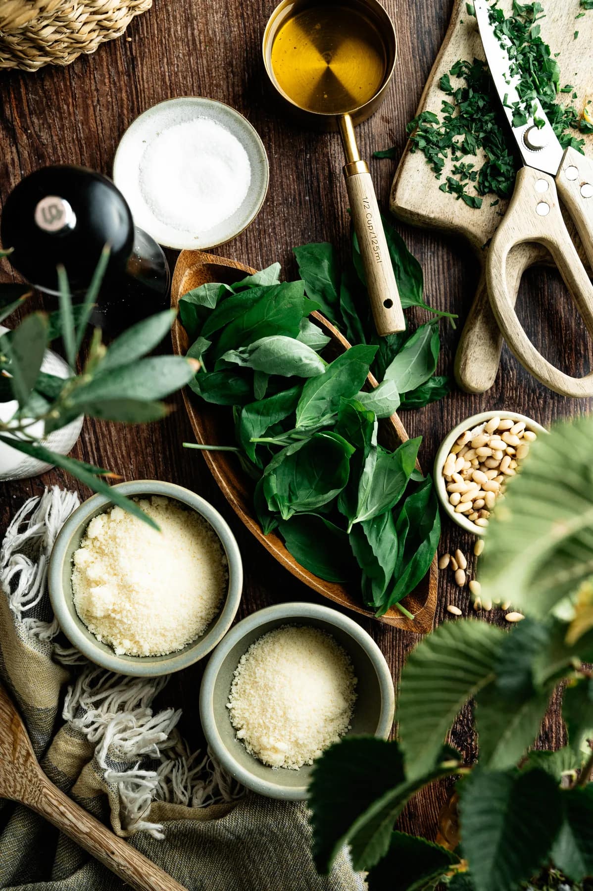 Basil leaves, pine nuts, grated cheese, olive oil and salt arranged on a wooden table.