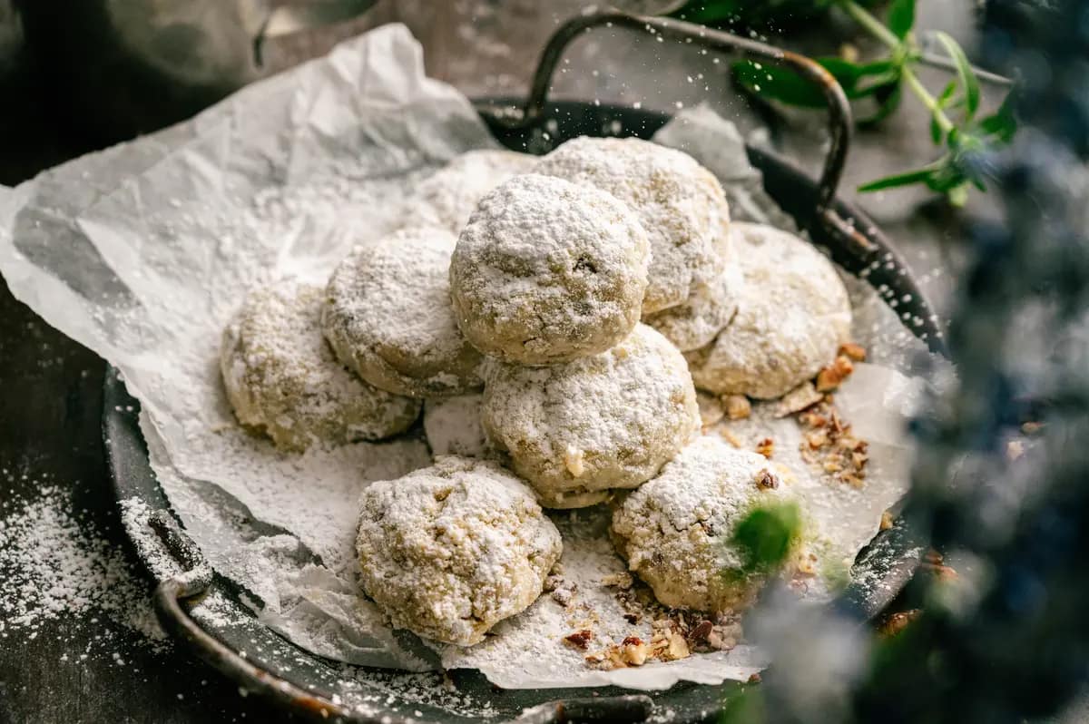 Pecan snowball cookies coated in powdered sugar on a parchment-lined dark tray.