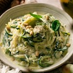 Lemon ricotta zucchini noodles topped with Parmesan, fresh basil, and toasted pine nuts in a shallow bowl.