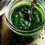 Close-up of a spoon resting in a jar of homemade basil pesto.