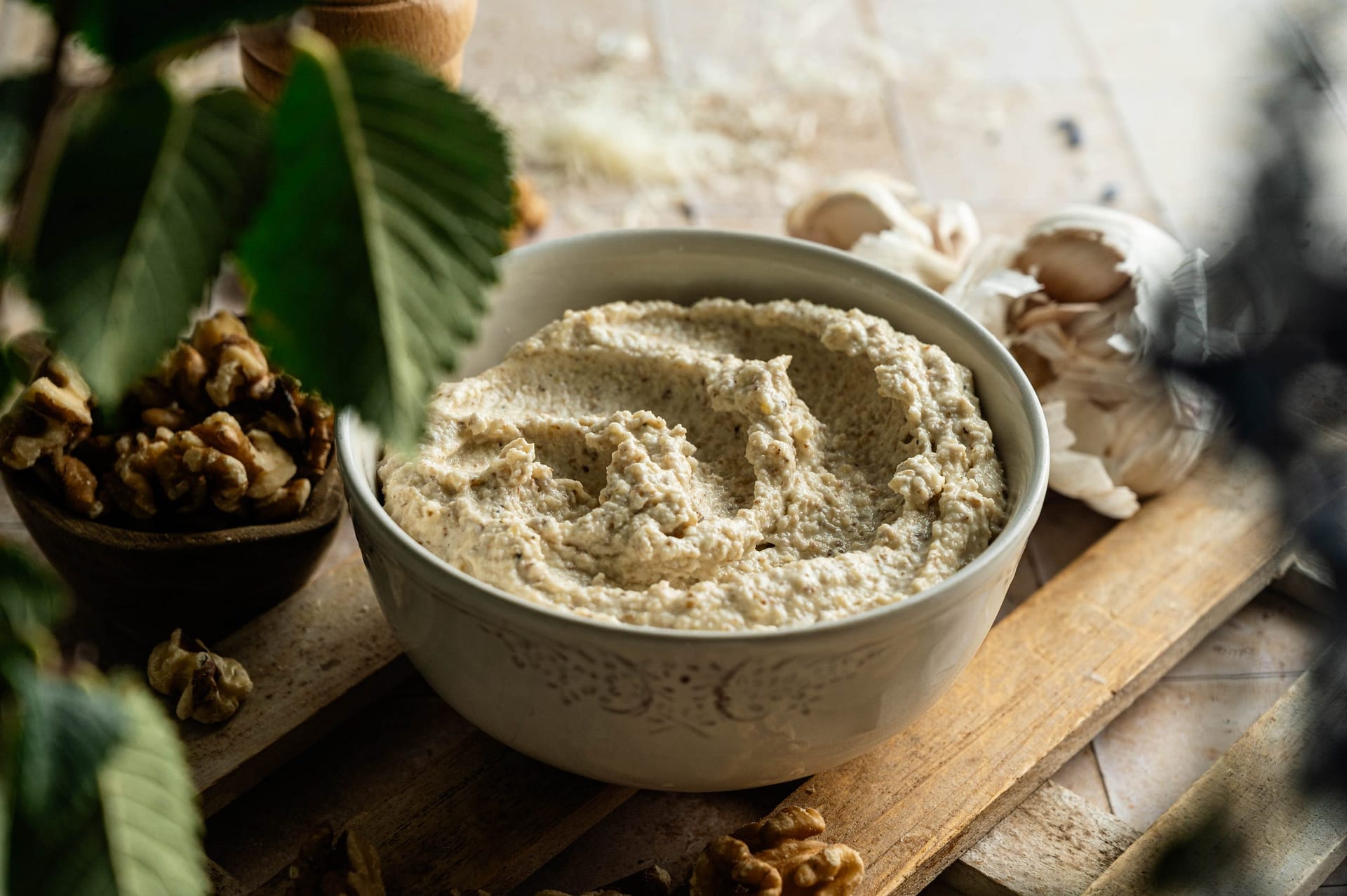 Side view of a bowl of thick, creamy Salsa di Noci on a wooden board.