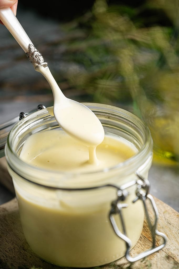 Hand holding a spoon as mayonnaise drips into a glass jar