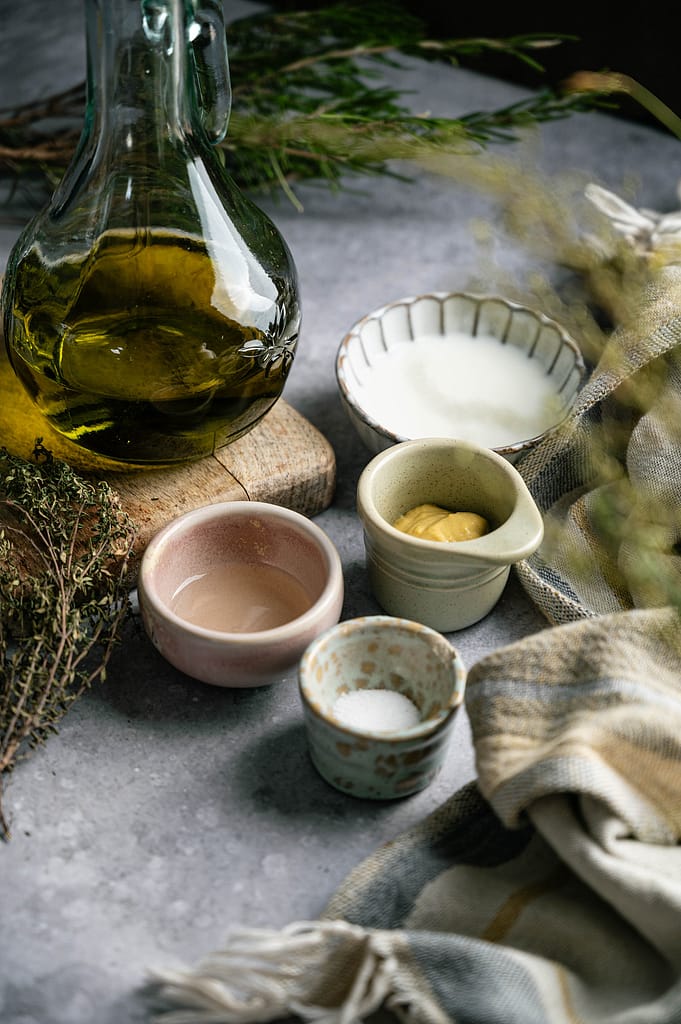 Bottle of oil and small ingredient dishes on a gray surface beside folded linen
