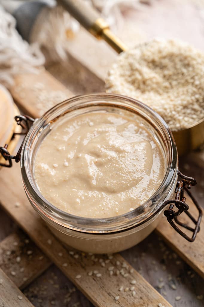 Close-up of pale, creamy homemade tahini with swirls on the surface in an open glass jar.