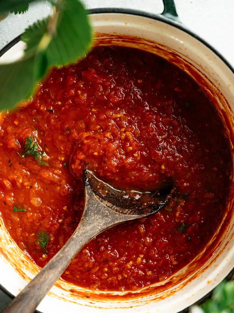 Rustic homemade marinara sauce with a metal ladle and fresh basil