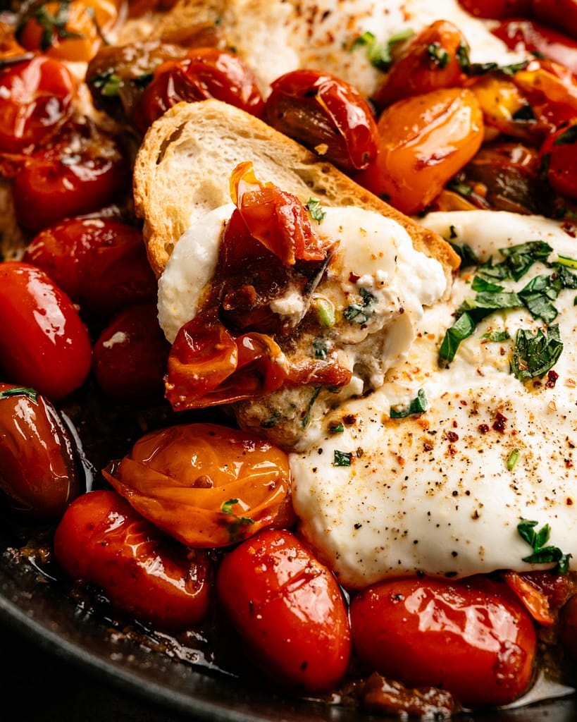 Close-up of creamy burrata with burst cherry tomatoes, fresh basil, and toasted bread.
