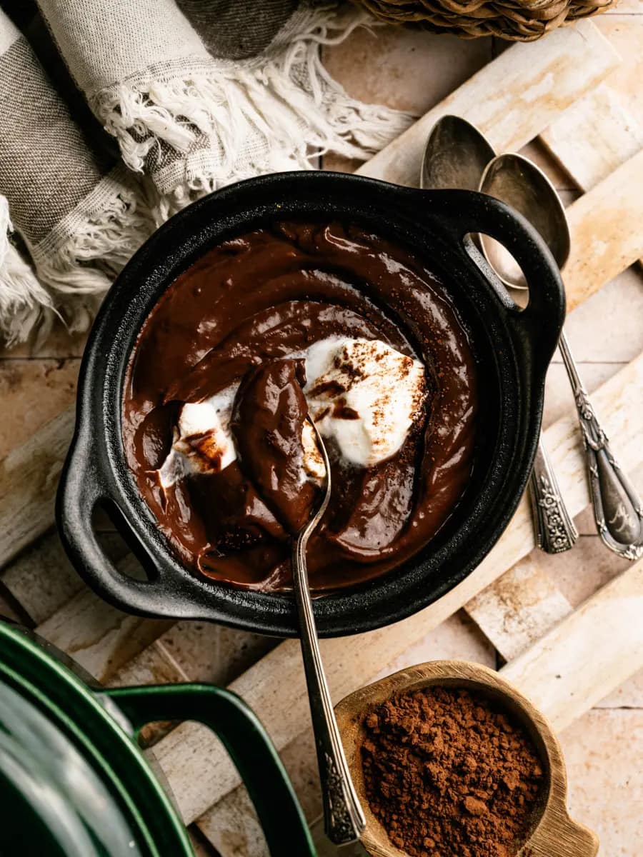 Spoon lifting creamy homemade chocolate pudding and whipped cream from a black bowl